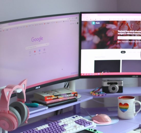 Stylish desk setup with dual monitors, keyboard, headphones, and cozy decor for tech enthusiasts.